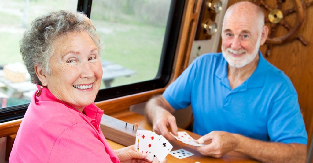 Seniorenpaar sitzt am Tisch in einem Wohnmobil und spielt Karten | Immobilienverrentung Leibrente
