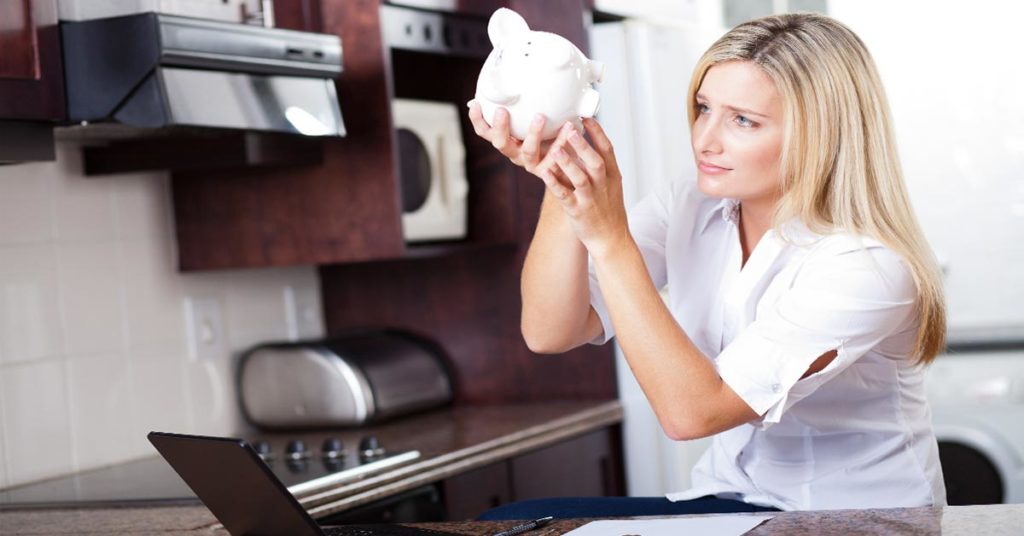 Eine Frau sitzt in der Küche und sucht in Ihrem Sparschwein nach Geld