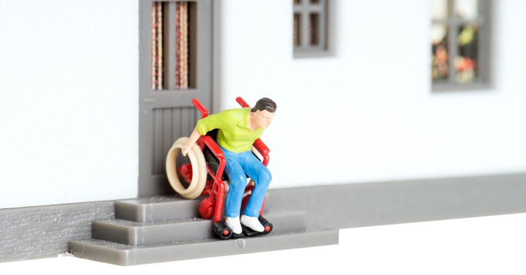 Ein Spielzeugmann in einem Rollstuhl fährt eine Spielzeugtreppe herunter - Wohnen im Alter